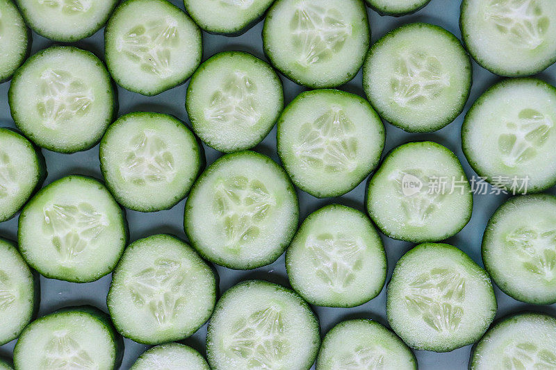 绿色背景上的一层黄瓜(Cucumis sativus)切片的全画幅图像，显示绿色的皮肤和白色的果肉与白色的种子，健康饮食海报壁纸背景设计，高架视图